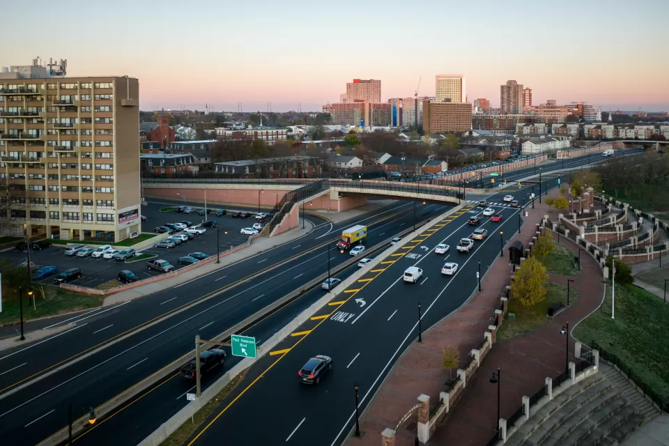 Overhead view of highway with offramps leading to overpass and buildings in the distance.